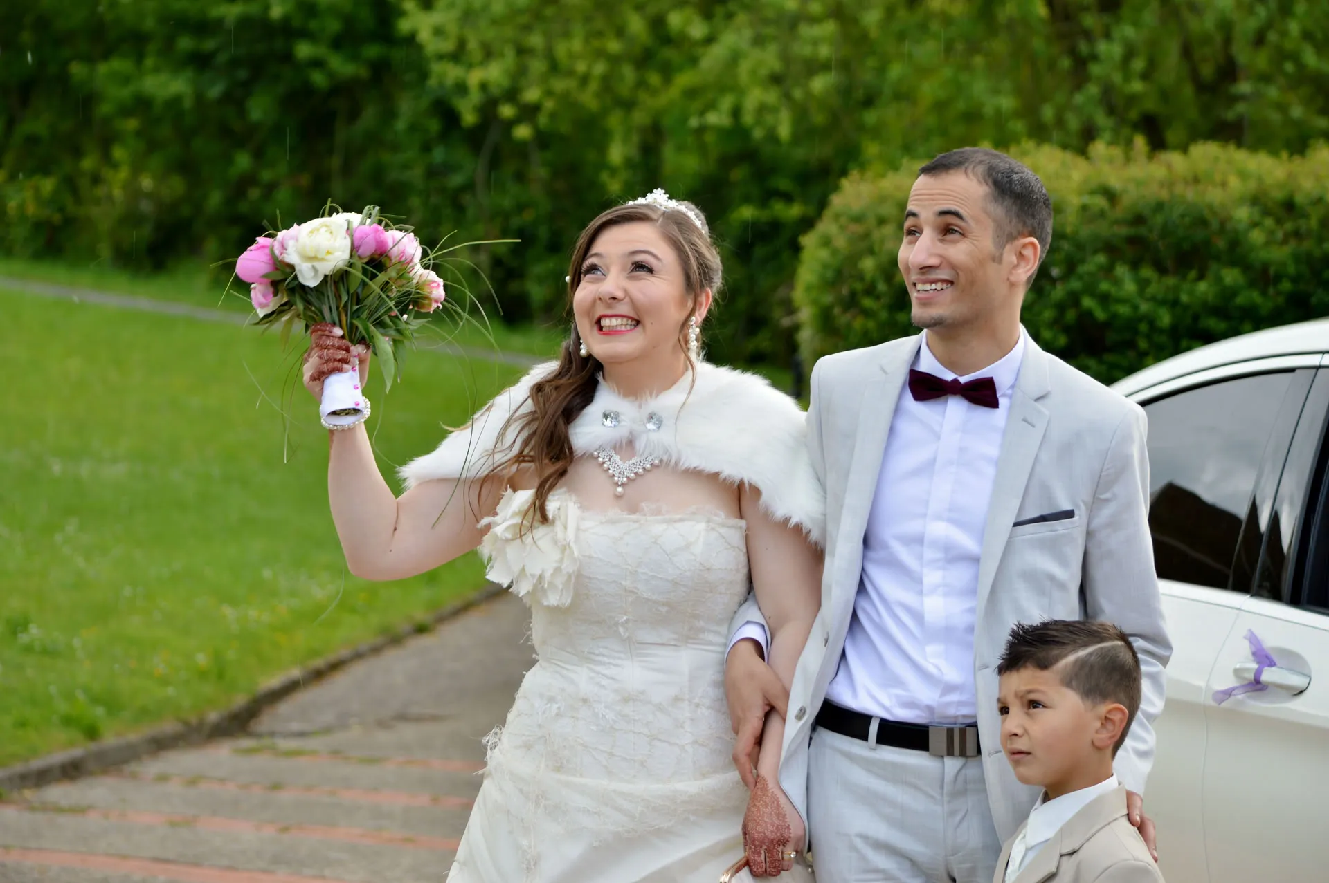 Mariage, le couple et un enfant à la sortie de voiture, il pleut, ils regardent en l'air en souriant
